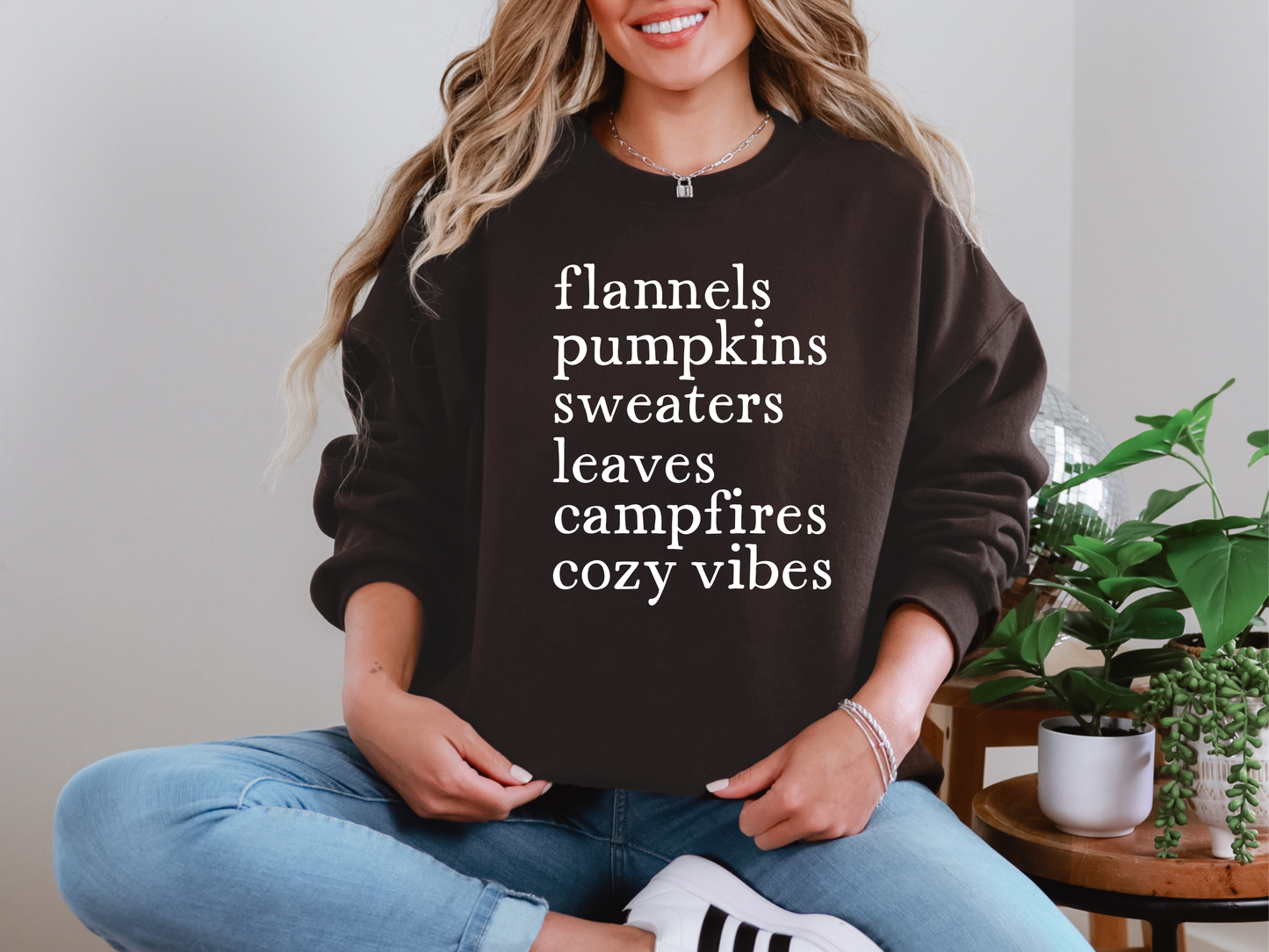 Person wearing a black sweatshirt with text, sitting indoors with plants in the background