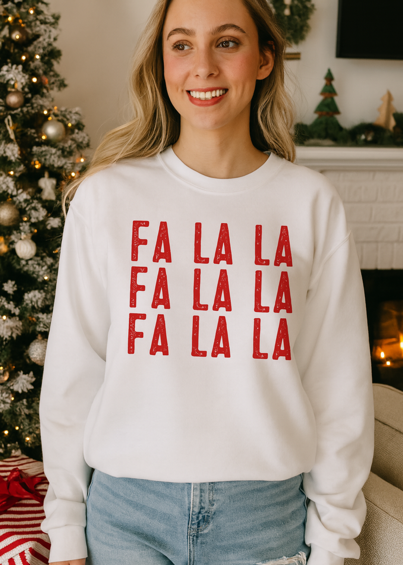 Woman wearing a white sweatshirt with red 'FA LA LA' text in a festive indoor setting.