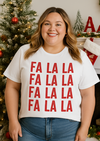 Person wearing a white t-shirt with 'FA LA LA' text in front of a Christmas tree.