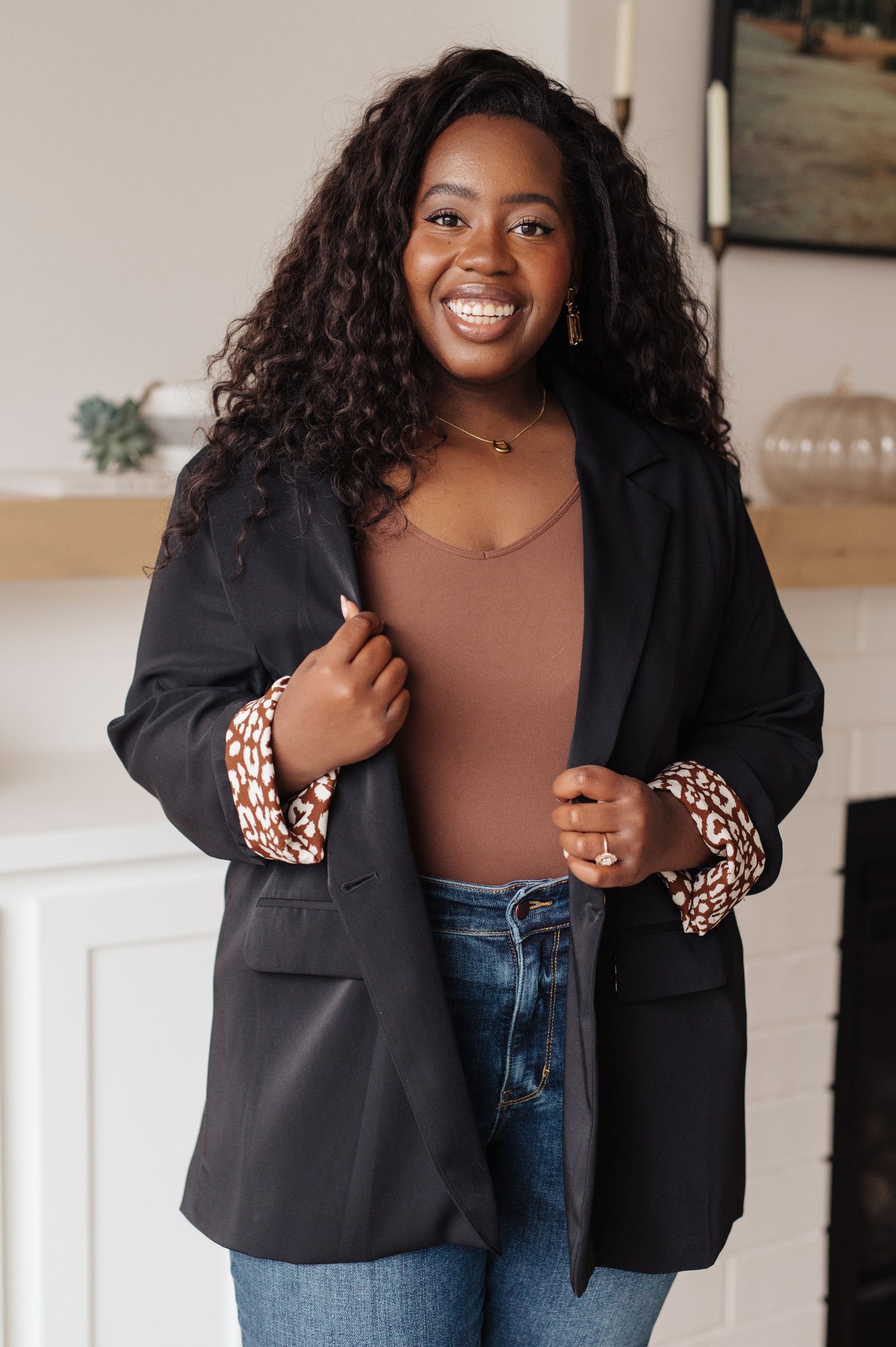 Woman wearing a black blazer over a brown top and blue jeans indoors.