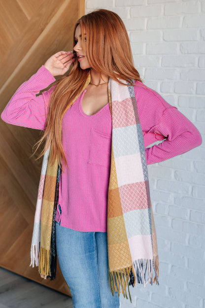 Woman wearing a pink sweater and colorful scarf against a white brick wall.