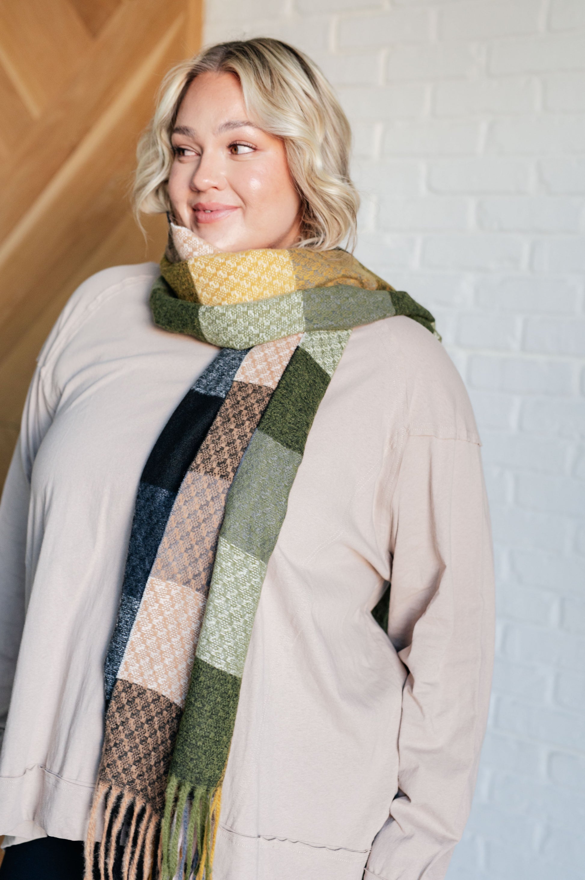 Woman wearing a patchwork scarf against a white brick wall.