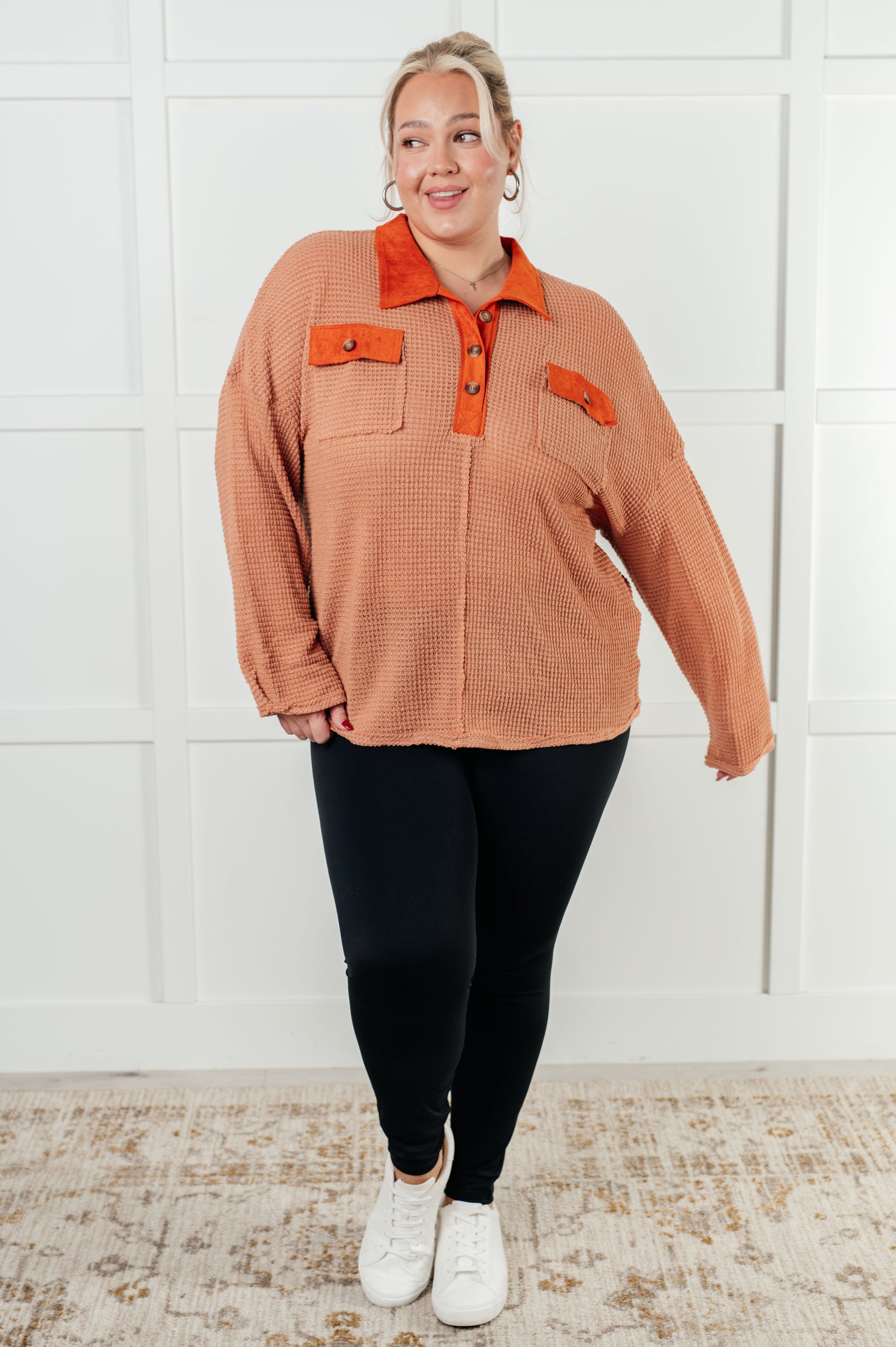Person wearing a brown corduroy shirt with orange accents against a white wall.