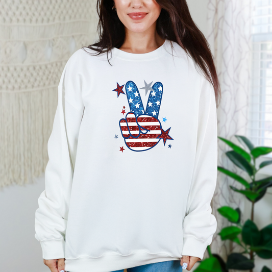 A woman wearing a white sweatshirt with a graphic of a peace sign and stars and stripes pattern.