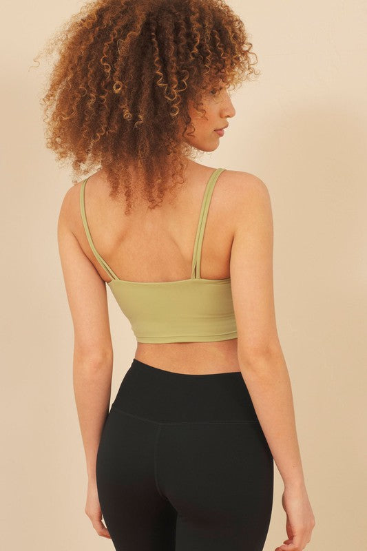 Woman wearing a green sports bra and black leggings against a beige background