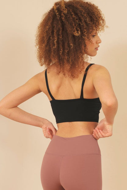 Woman wearing a black sports bra and pink leggings against a beige background