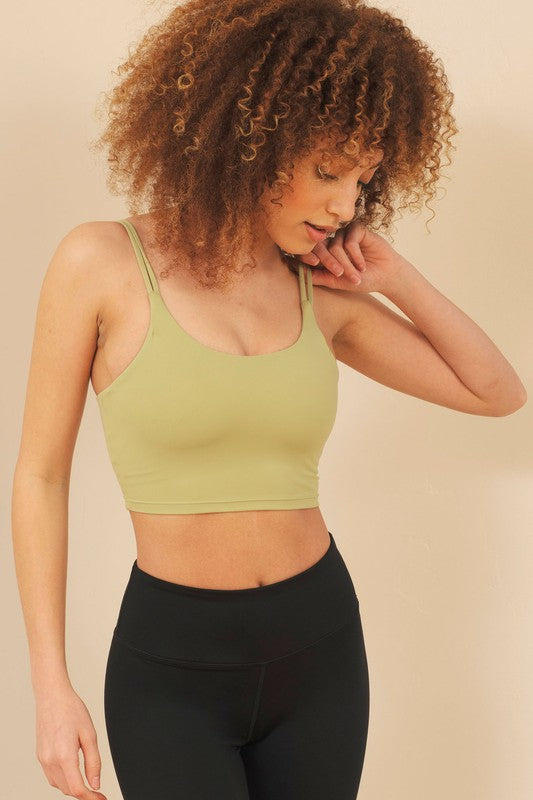 Woman wearing a green sports bra and black leggings against a beige background