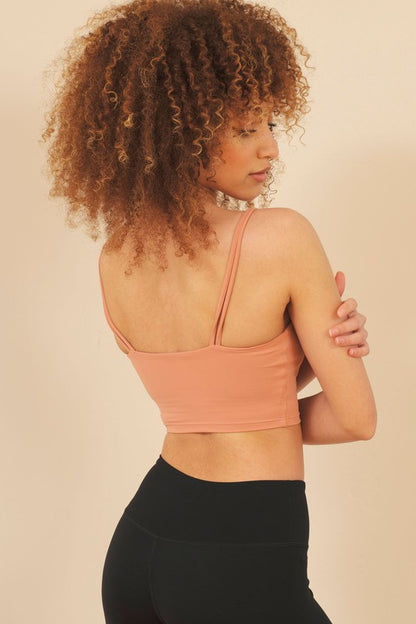 Woman wearing a peach sports bra and black leggings against a beige background