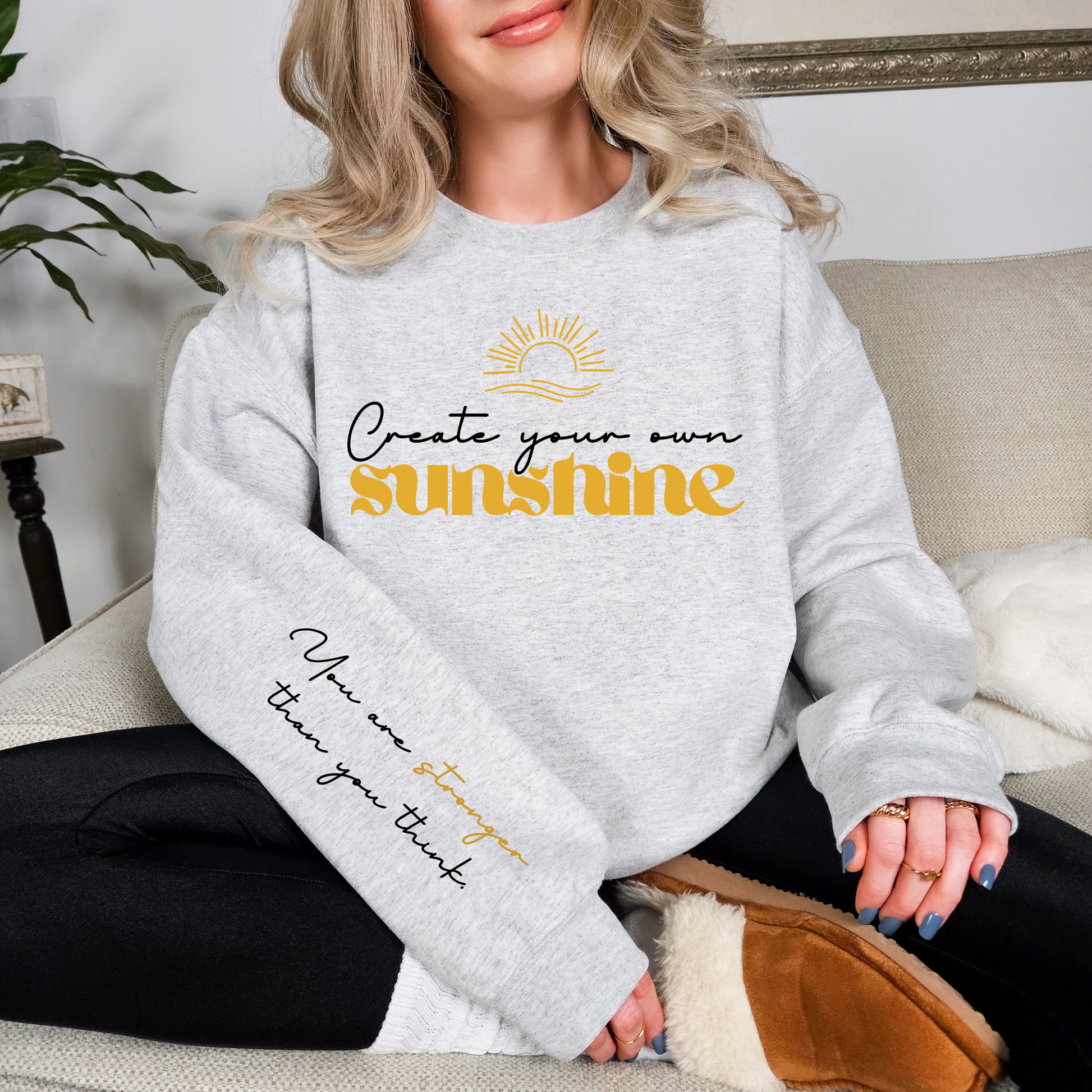 Person wearing a sweatshirt with 'Create your own sunshine' text, sitting on a couch.