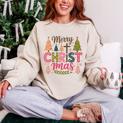 Person wearing a Christmas-themed sweatshirt with a tree and candy cane design, sitting in front of a decorated Christmas tree.