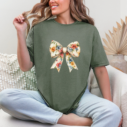 A woman sitting on a chair wearing a green graphic tee with a floral bow design on the front.