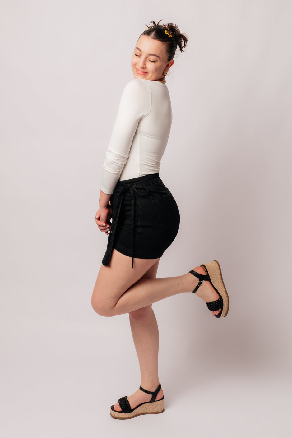 A person wearing a high rise side tie denim skort in black color with a self-tie side closure.