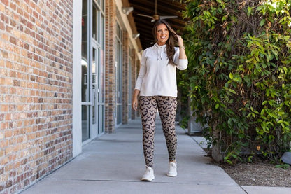 Woman in a white shirt and patterned leggings standing on a sidewalk next to a brick building.