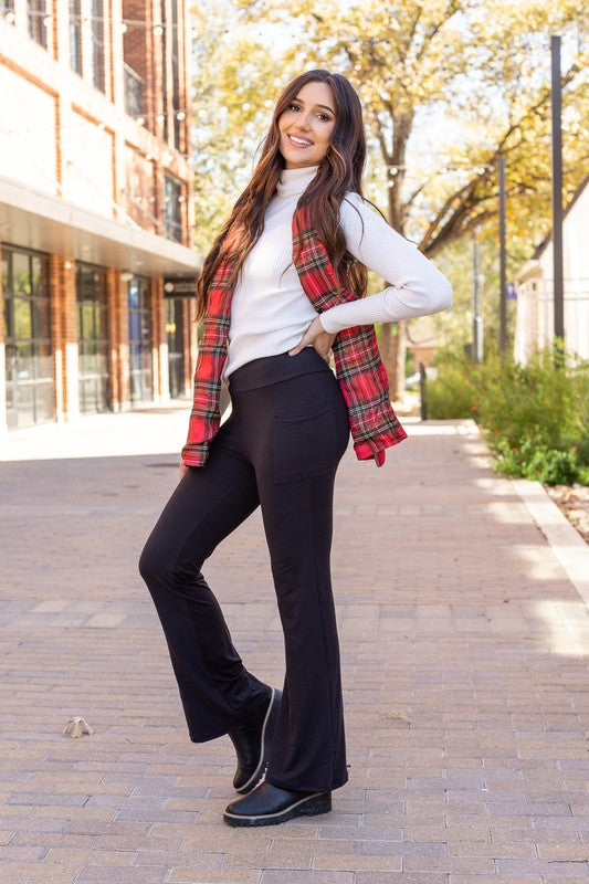 Woman wearing a plaid shirt over a white sweater with black pants on a sidewalk.