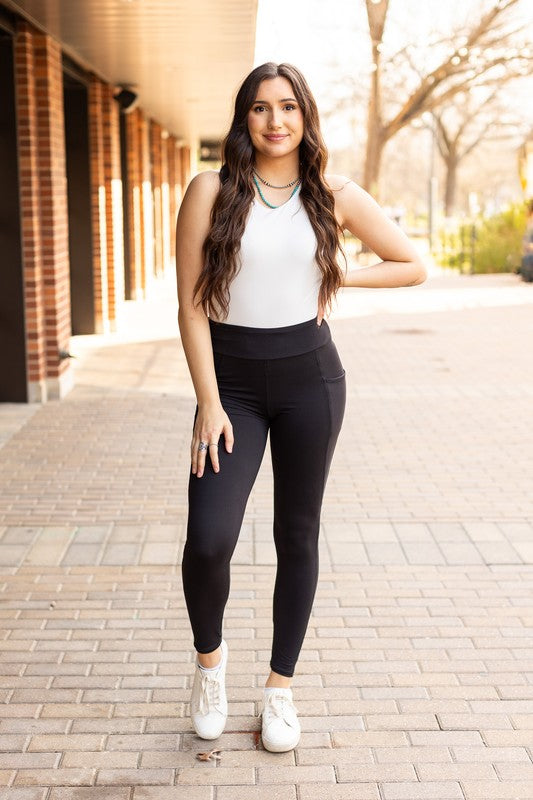 Woman wearing a white top and black leggings standing on a sidewalk.
