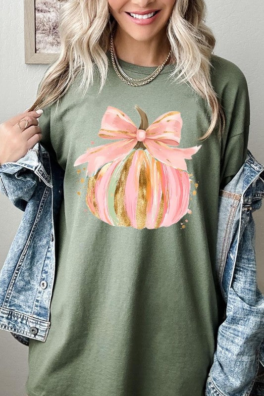 Woman wearing a green shirt with a pink and gold pumpkin design, standing indoors.