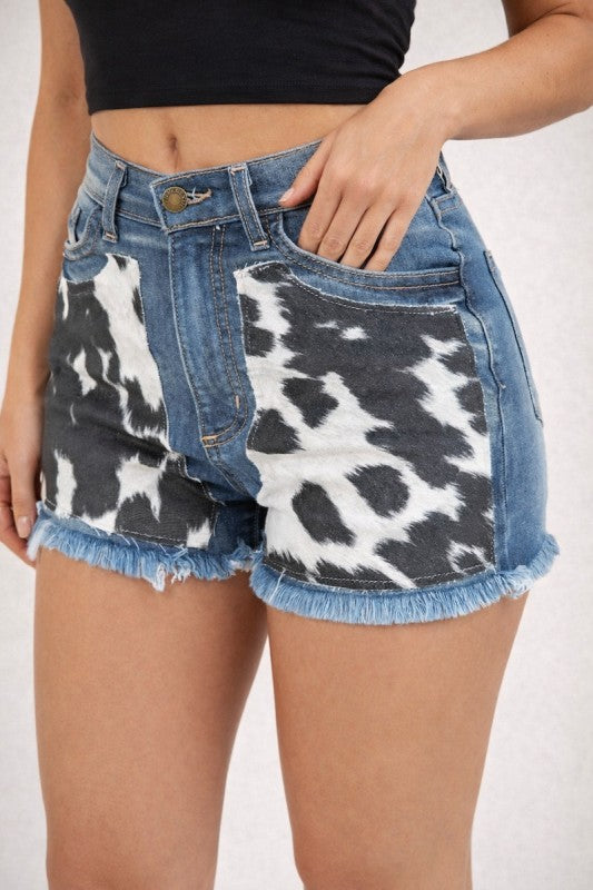 Denim shorts with cow print pattern worn by a person on a white background
