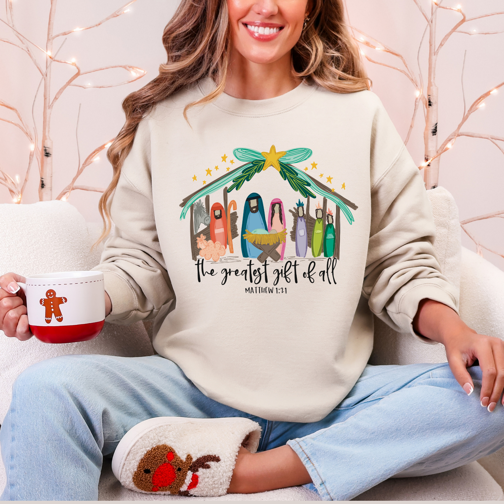 Person wearing a Christmas-themed sweatshirt with a nativity scene design, holding a mug.