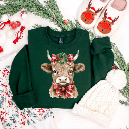 Green sweatshirt with a cow design wearing a red bow, surrounded by Christmas decorations.