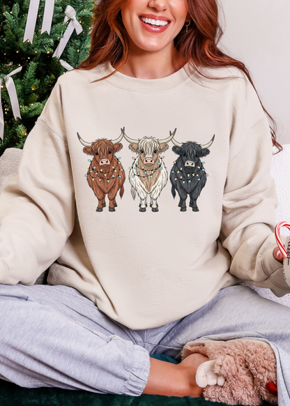 Person wearing a beige sweatshirt with cow illustrations in front of a decorated Christmas tree.