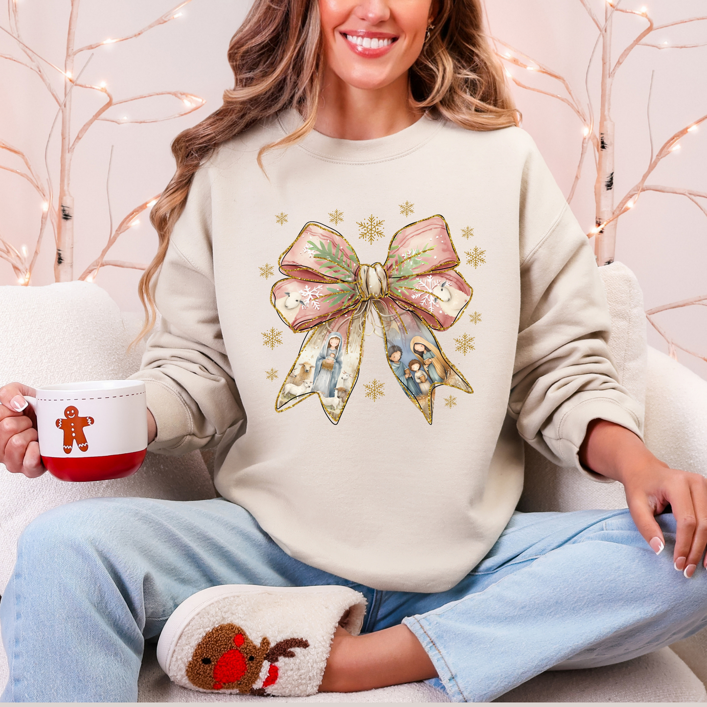 Person wearing a cream sweatshirt with a decorative bow design, holding a mug and sitting on a couch.