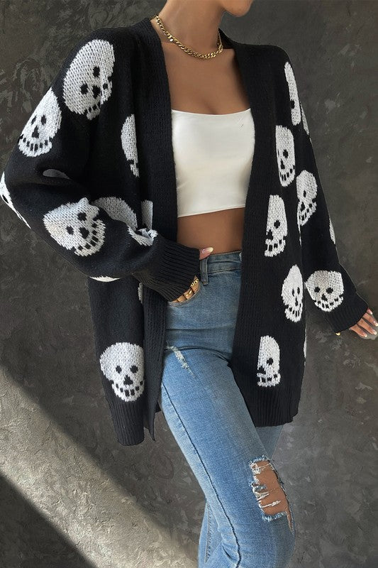 Person wearing a black cardigan with skull patterns, white top, and blue jeans.