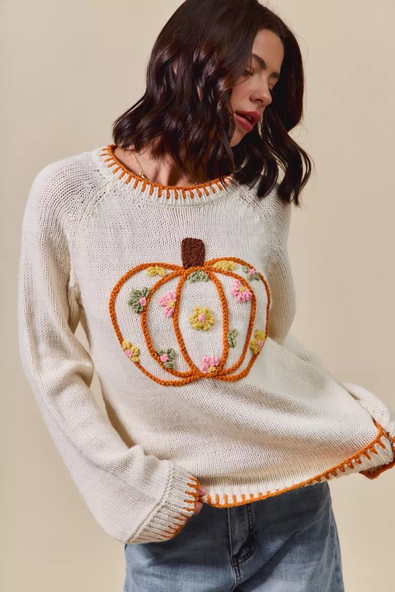 Woman wearing a cream sweater with a decorative pumpkin design on a beige background