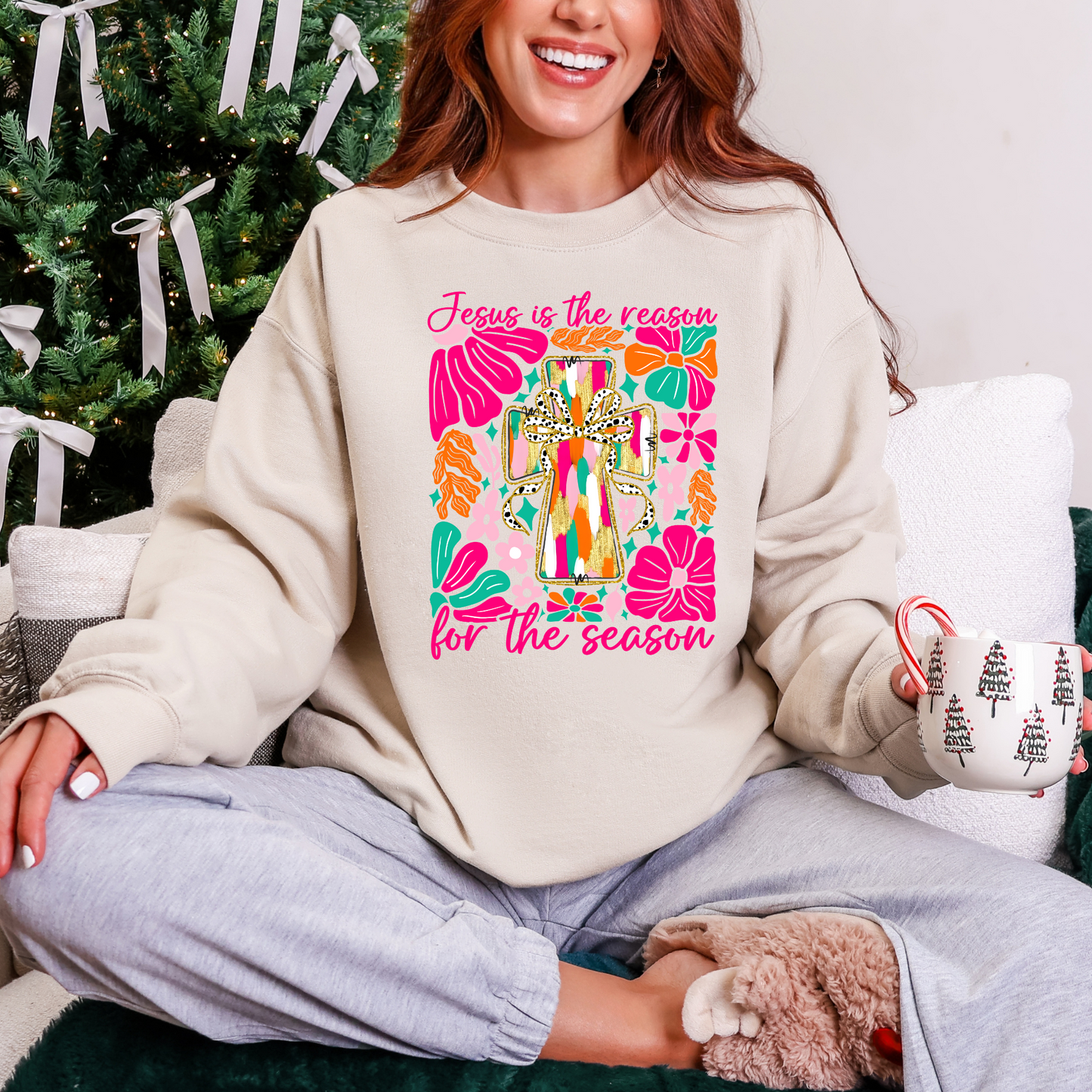 Person wearing a sweatshirt with a colorful design and text, sitting in front of a decorated Christmas tree.