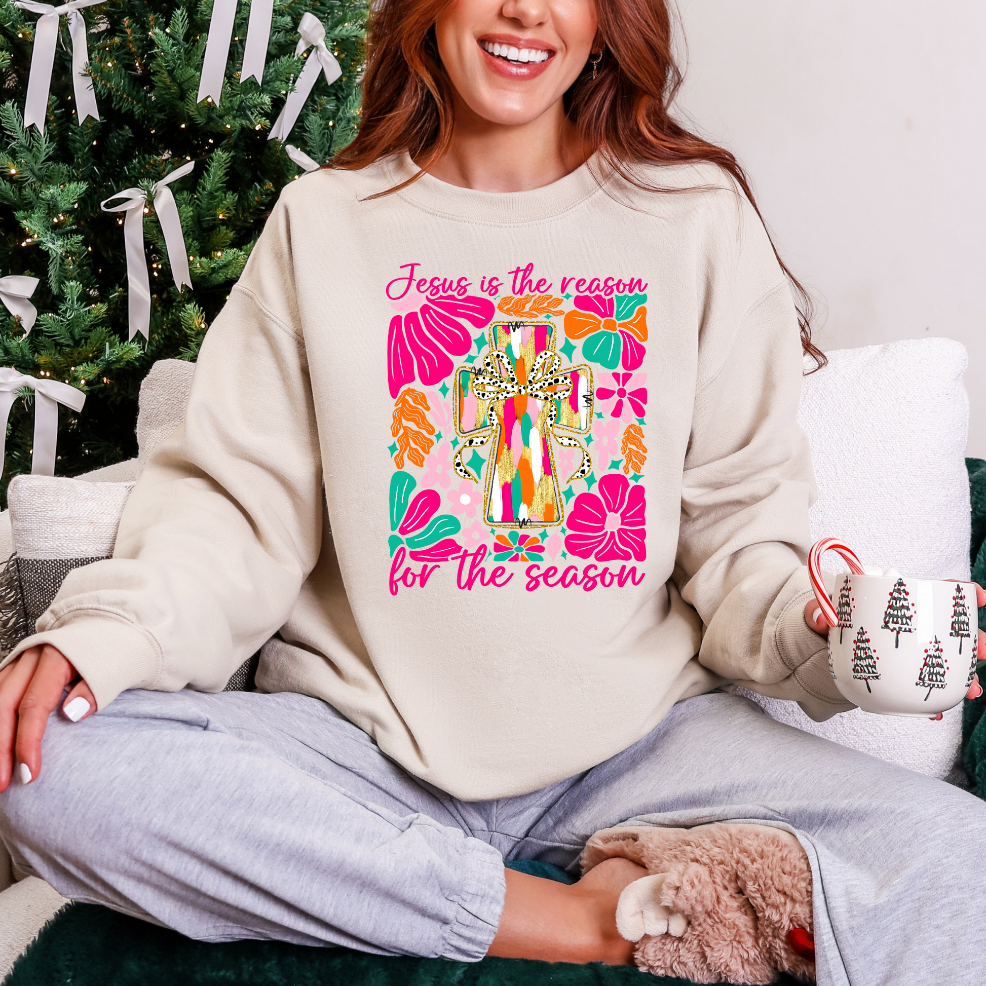Person wearing a sweatshirt with a colorful design and text, sitting in front of a decorated Christmas tree.