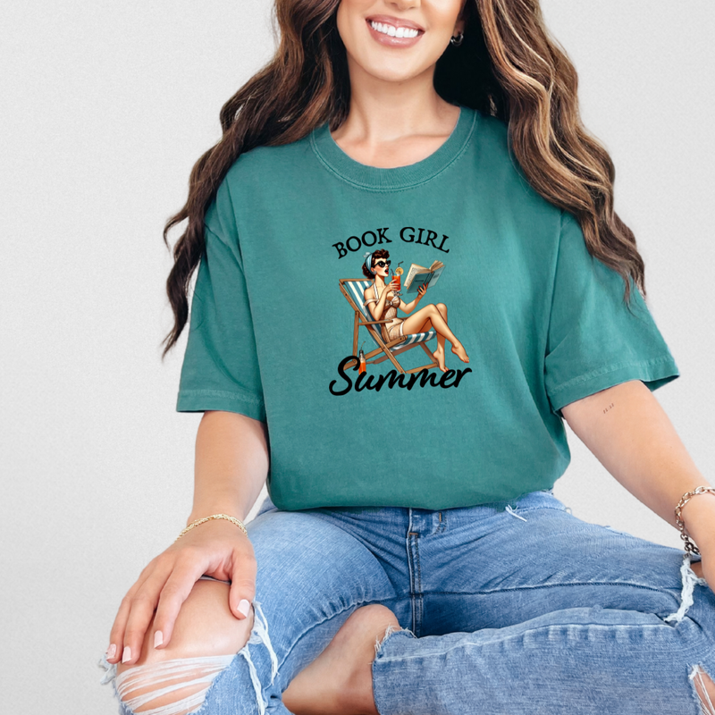 A woman sitting and smiling, wearing a green graphic tee with the text 'BOOK GIRL Summer' and an illustration of a girl with a book.