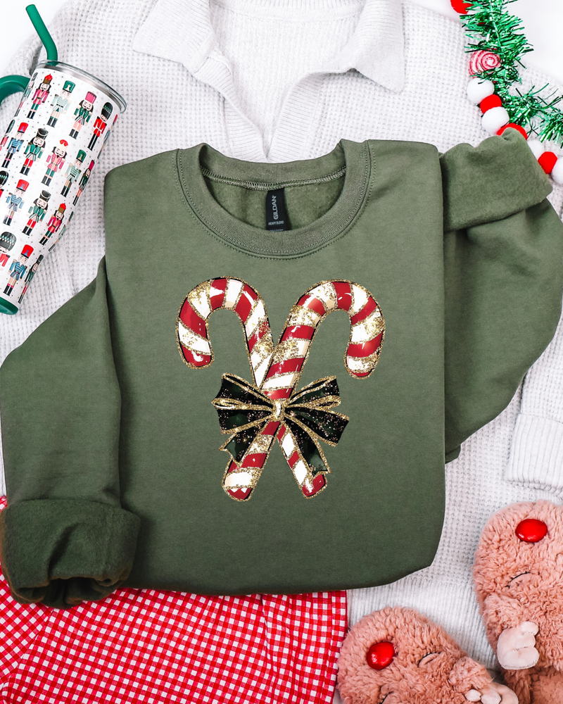 Green sweatshirt with candy cane design on a festive background with tinsel and mug.