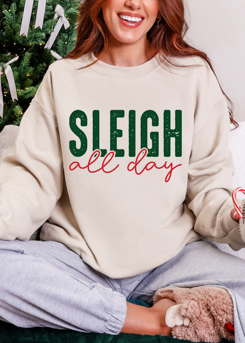 Person wearing a sweater with 'Sleigh all day' text, sitting in front of a decorated Christmas tree.