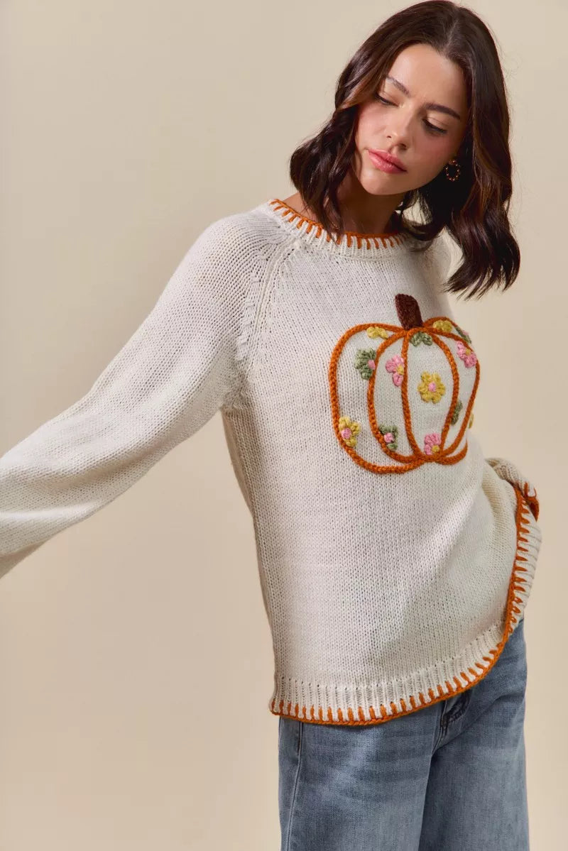Woman wearing a cream sweater with a decorative pumpkin pocket on a beige background