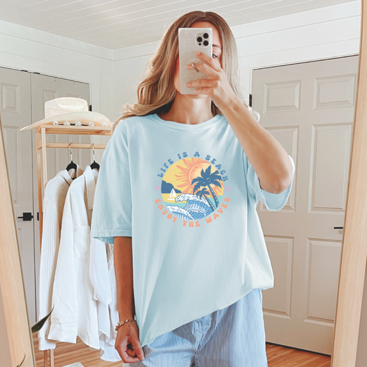 A person taking a mirror selfie wearing a blue graphic tee with a sun and beach-related design.