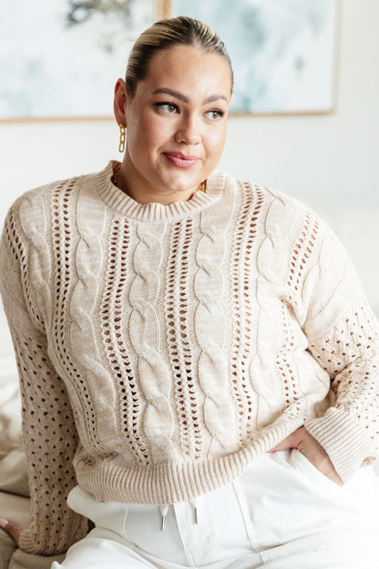 Woman wearing a beige cable knit sweater in a bright room