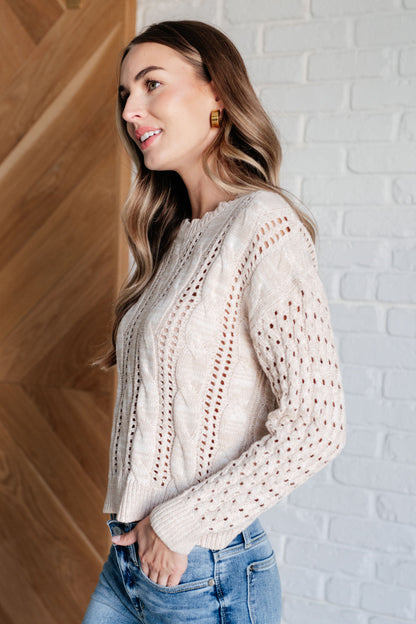 Woman wearing a cream sweater and blue jeans against a white brick wall.