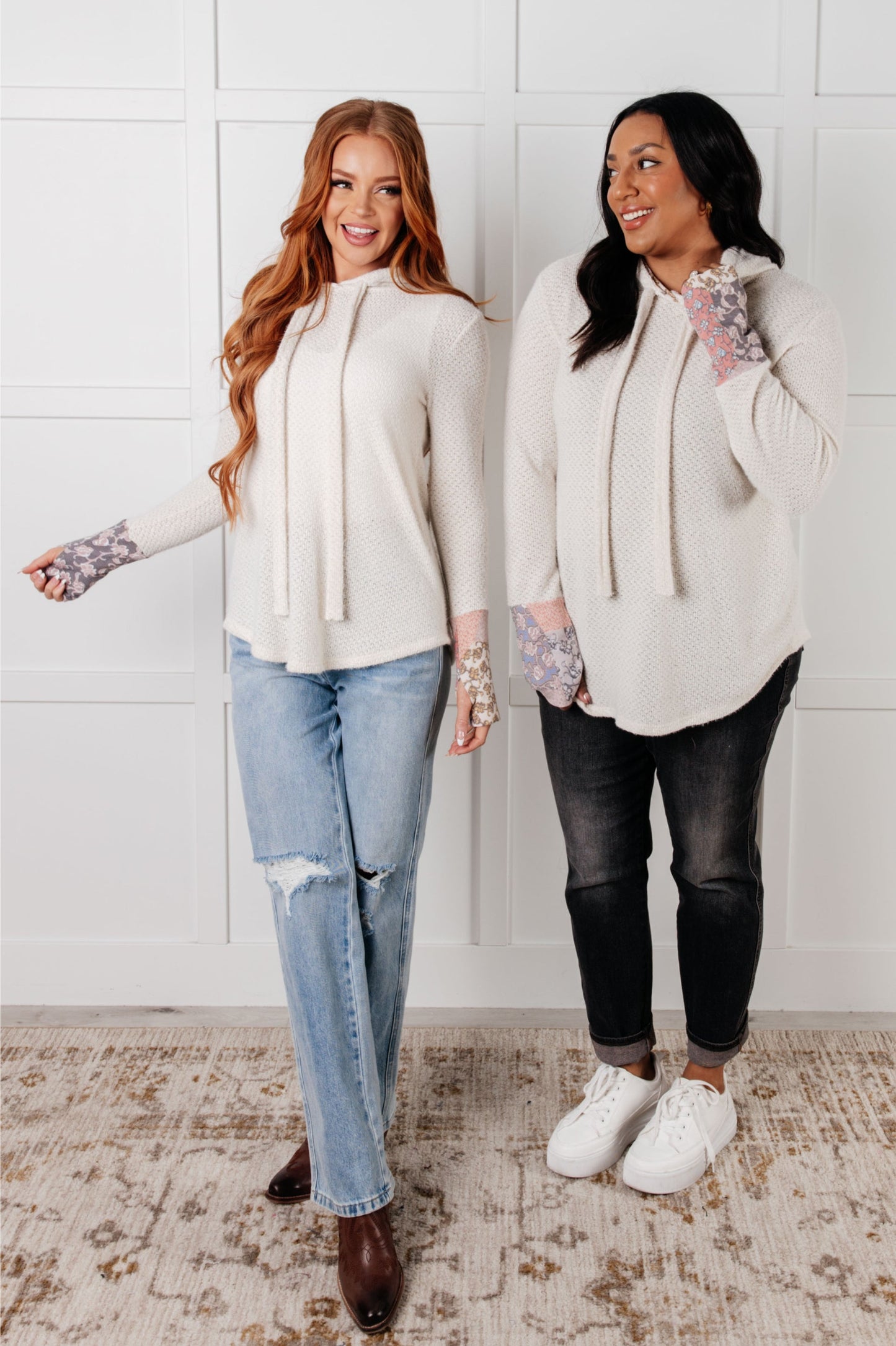 Two women wearing white cardigans in a room with a white wall.