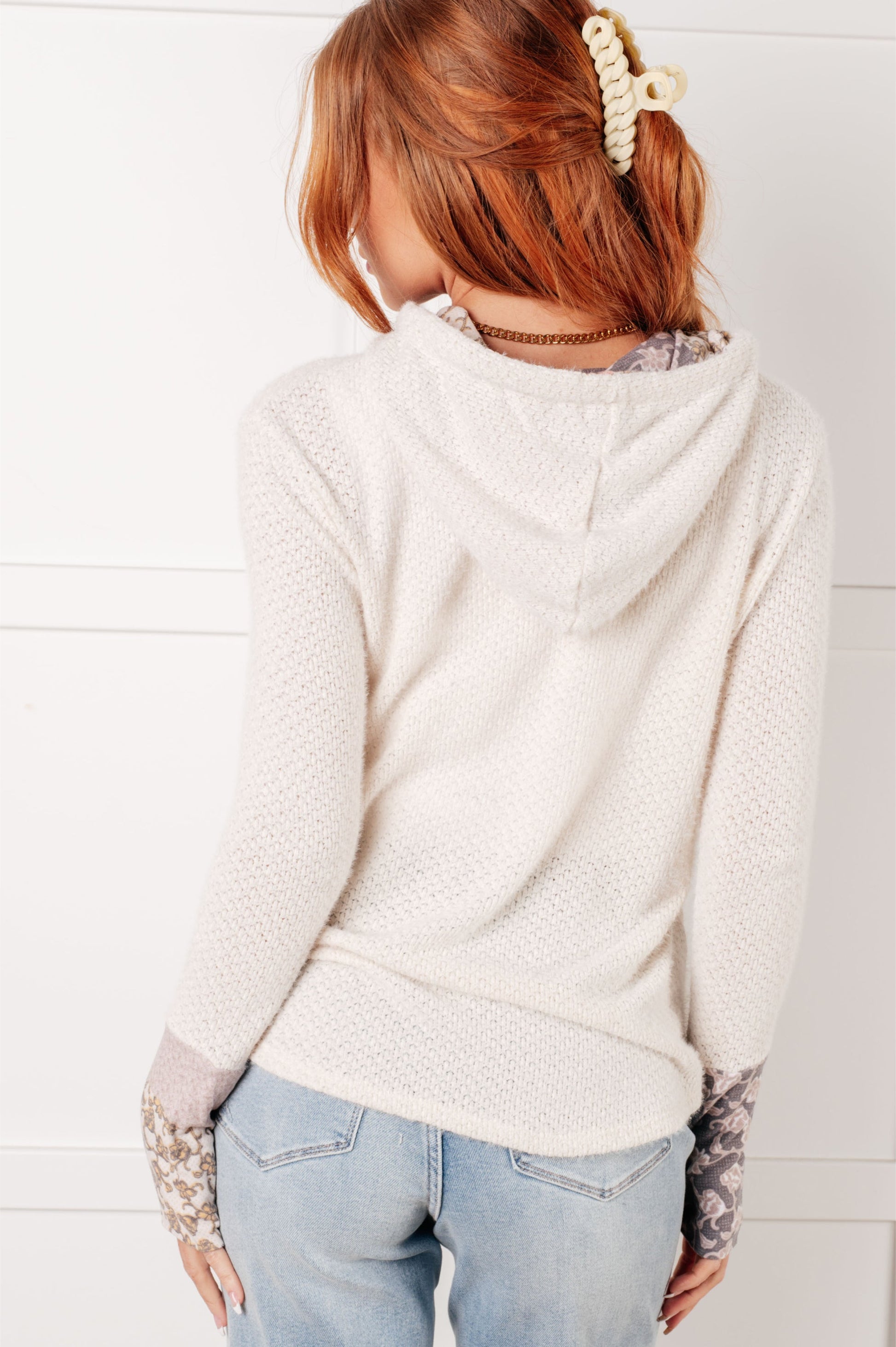 Person wearing a light-colored hoodie with patterned sleeves against a white background