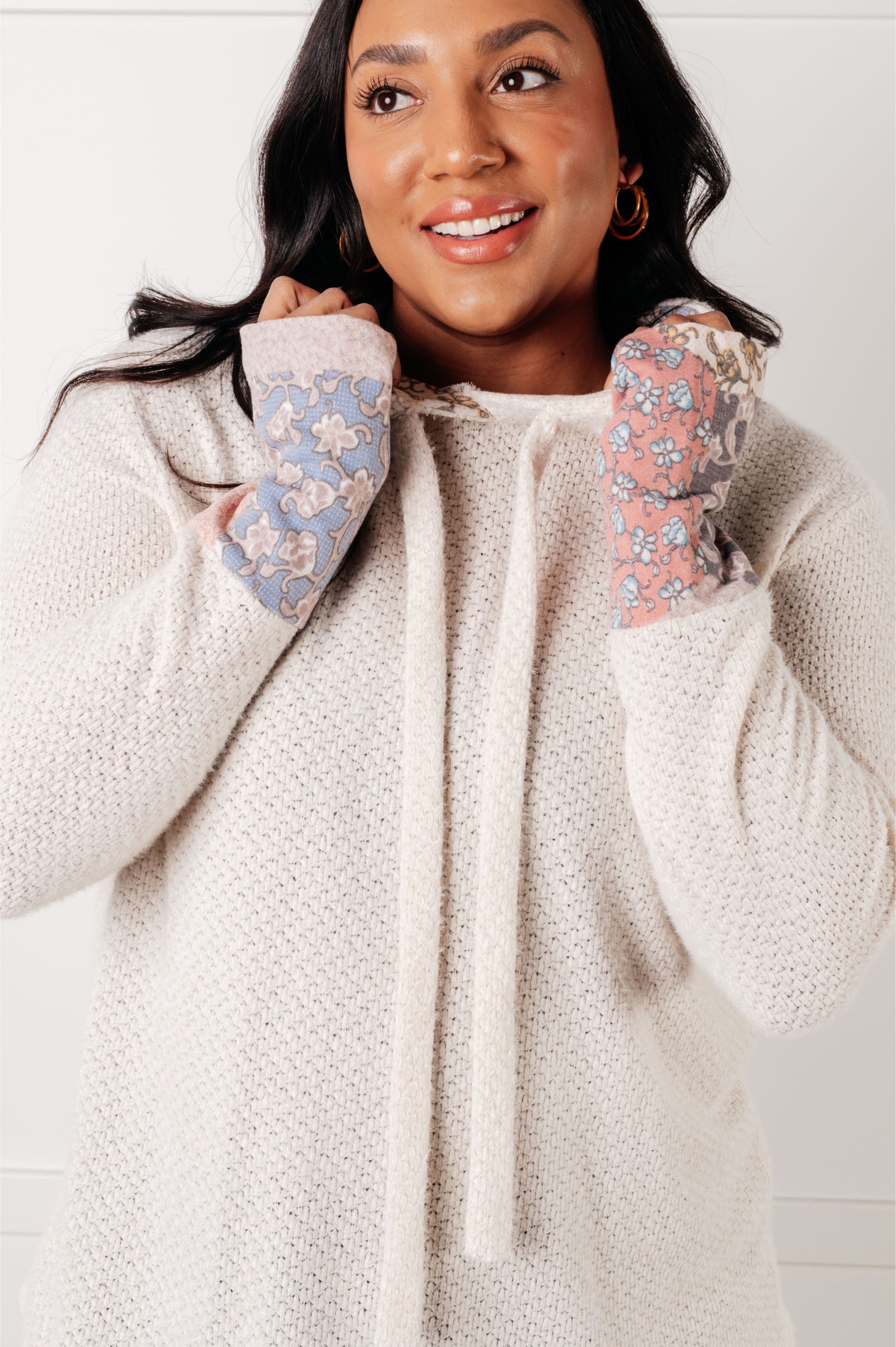 Woman wearing a cream-colored hoodie with floral sleeves against a white background