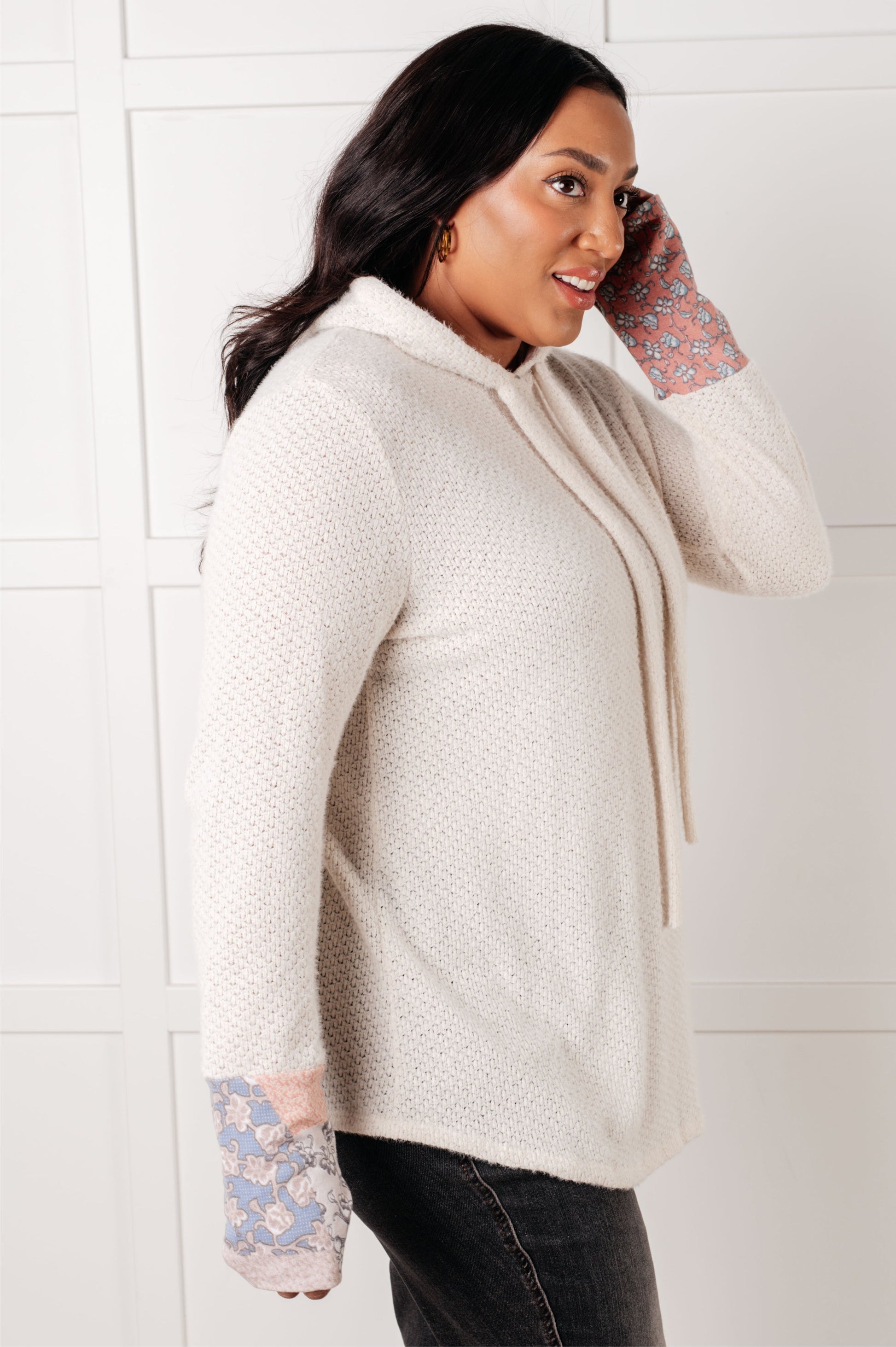 Woman wearing a cream-colored sweater with floral cuffs against a white background