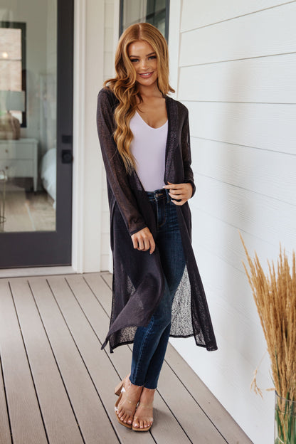 Woman wearing a long dark cardigan over a white top and jeans on a wooden deck.
