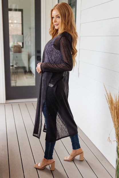 Woman wearing a long dark cardigan on a wooden deck.