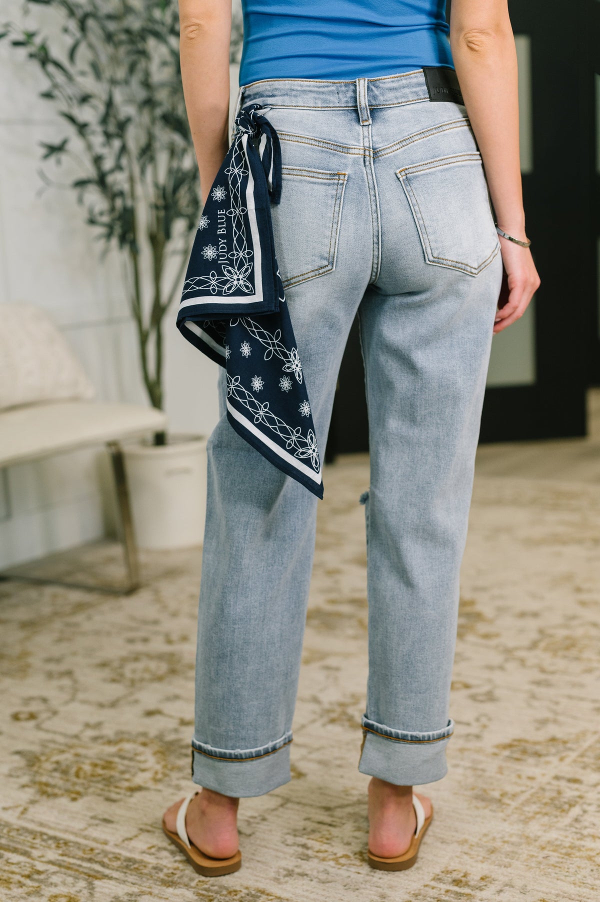 Person wearing light blue jeans with a bandana around their neck, standing on a textured floor.