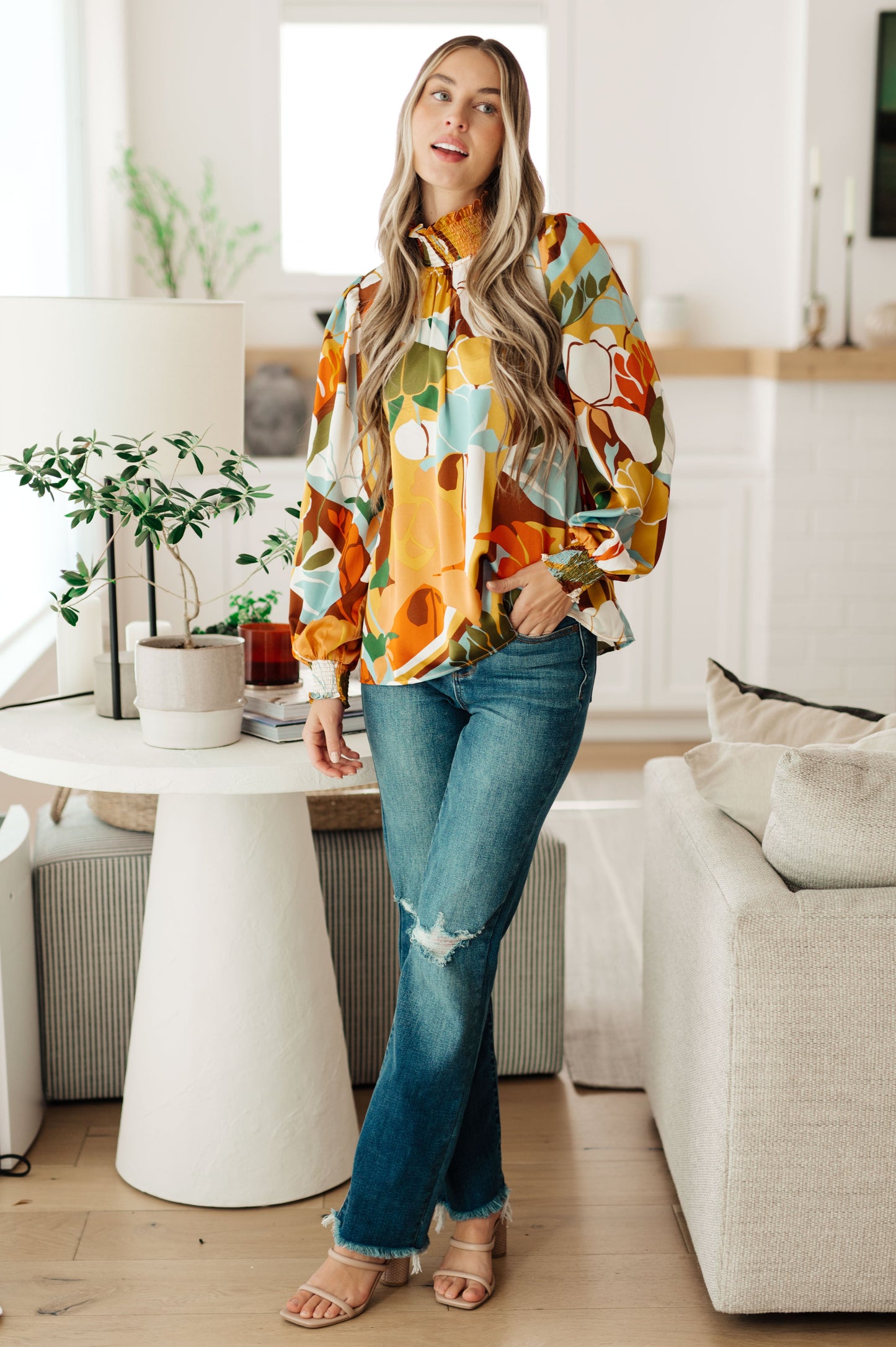 Woman in a colorful jacket and jeans standing in a modern living room.