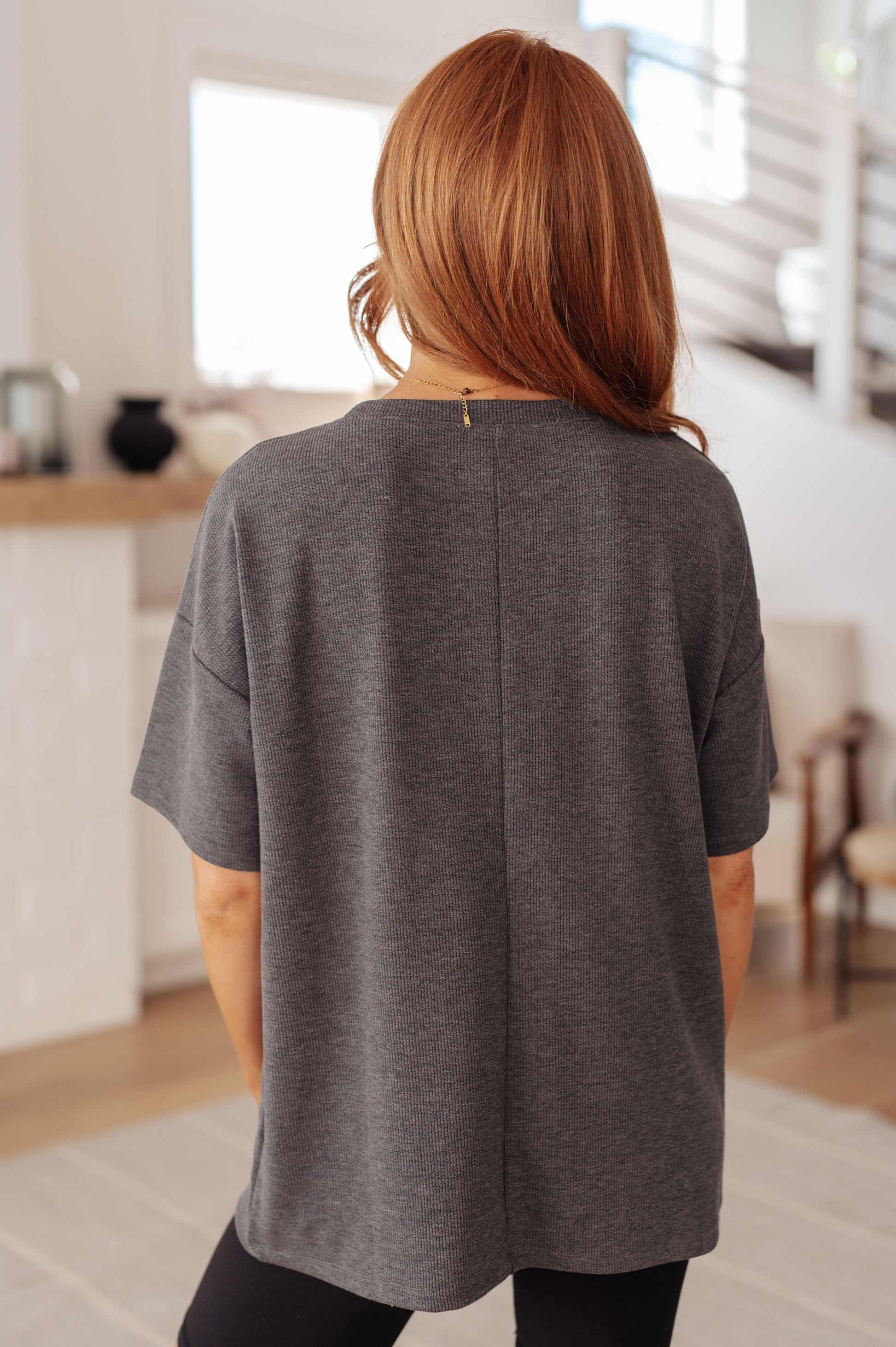 Person wearing a gray oversized t-shirt in a room with wooden flooring and white walls.