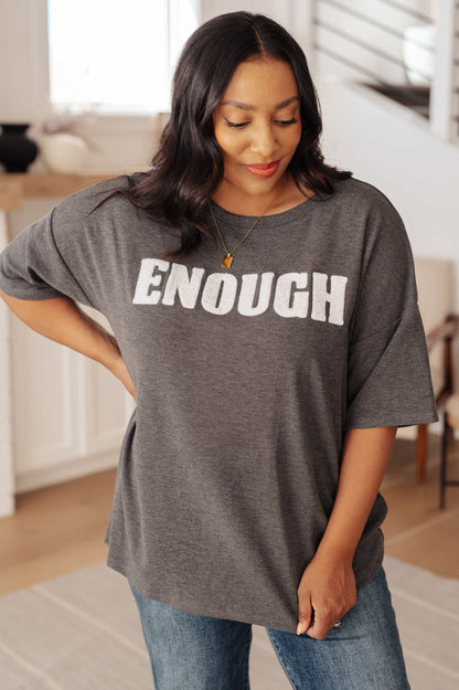 Woman wearing a gray t-shirt with 'ENOUGH' printed on it in a home setting.