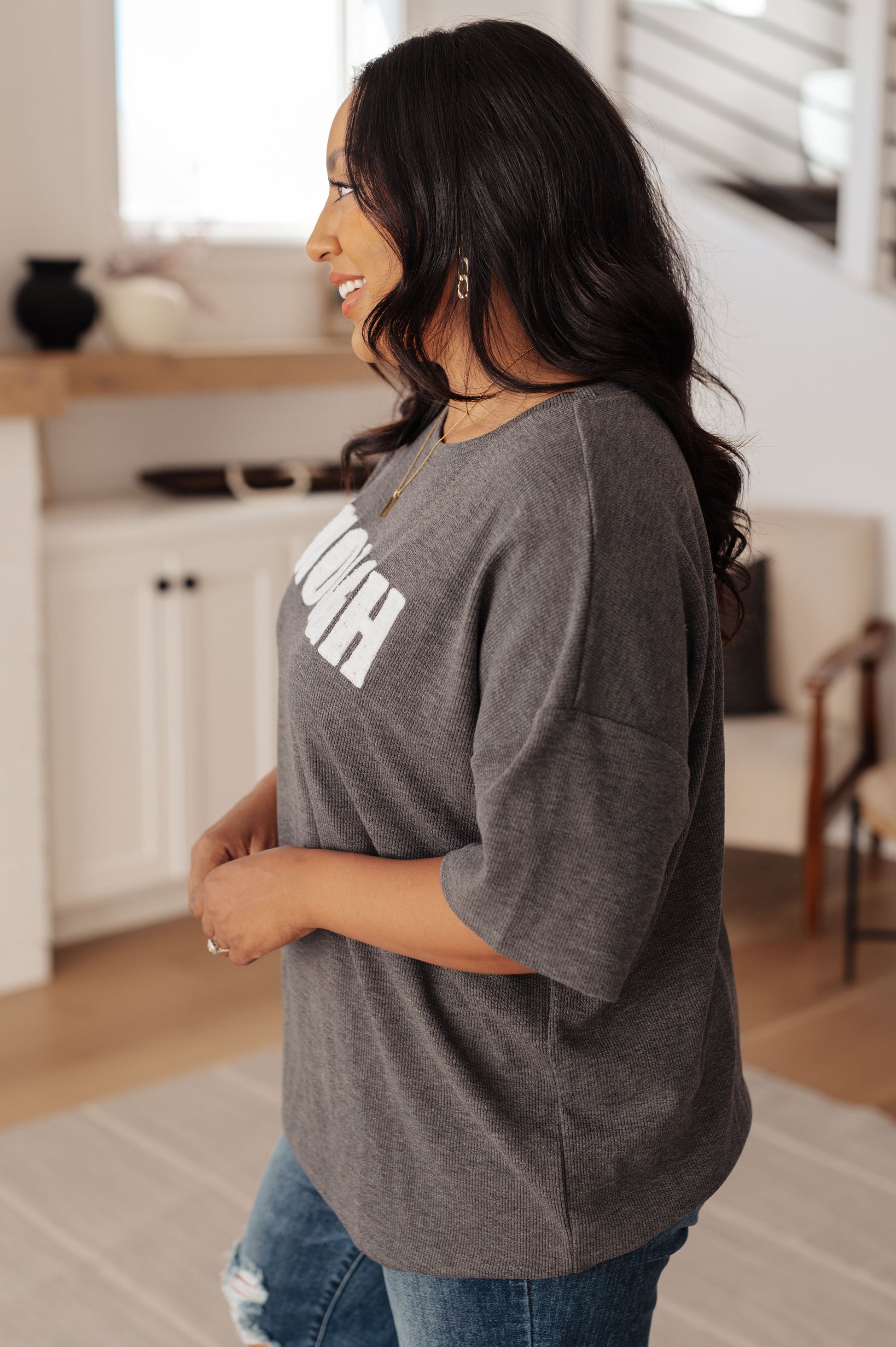 Woman wearing a gray oversized t-shirt with text in a kitchen setting