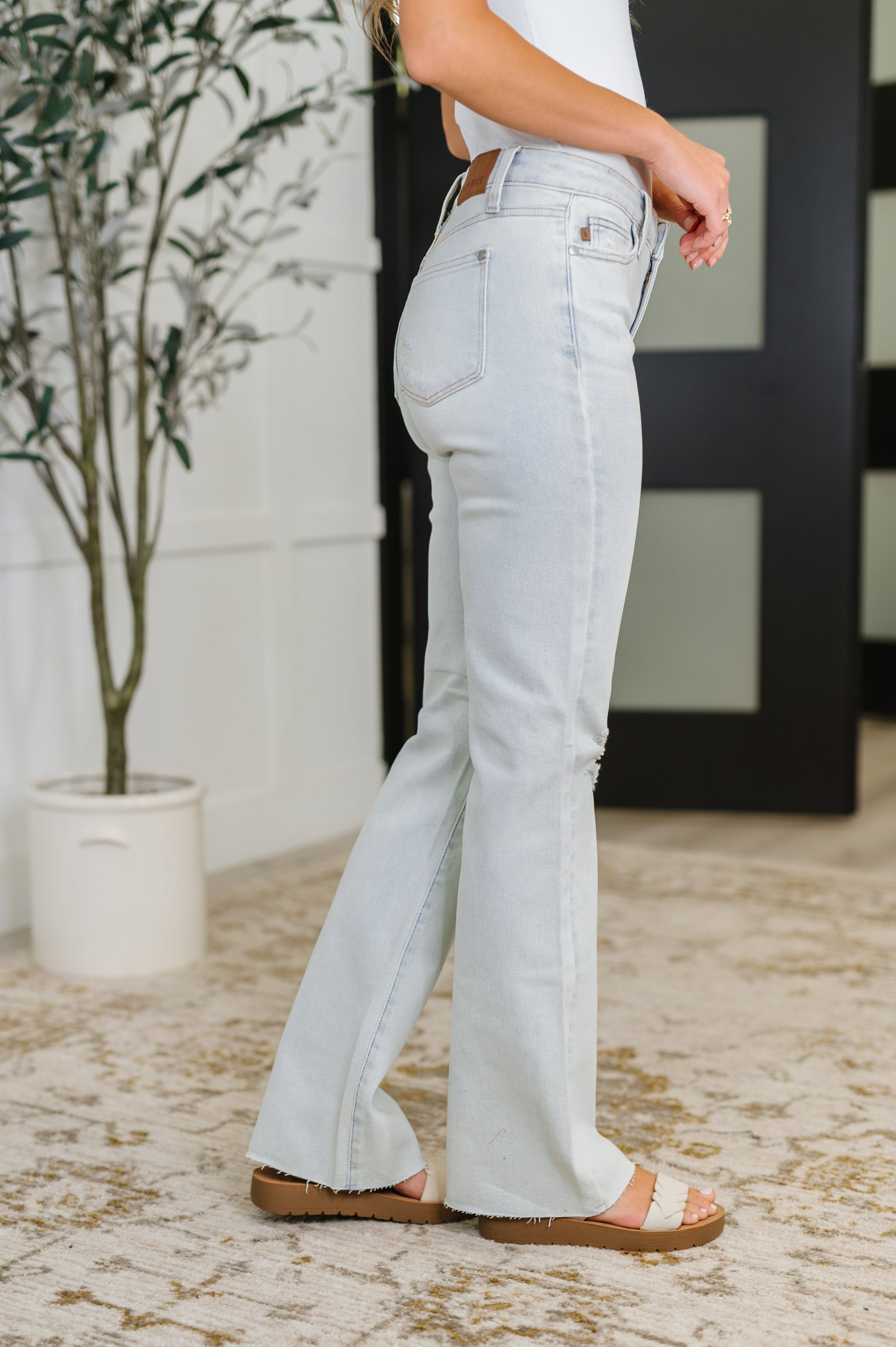 Light blue jeans worn by a person indoors with a plant and door in the background