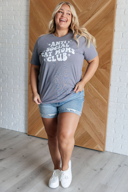 Woman wearing a gray t-shirt with text and denim shorts standing against a wooden wall.