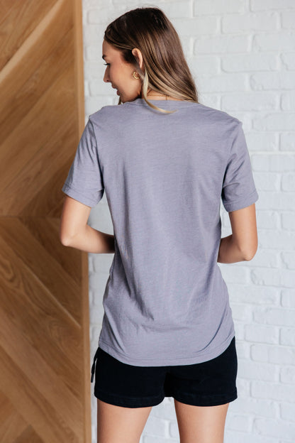 Woman wearing a gray t-shirt and black shorts against a white brick wall.